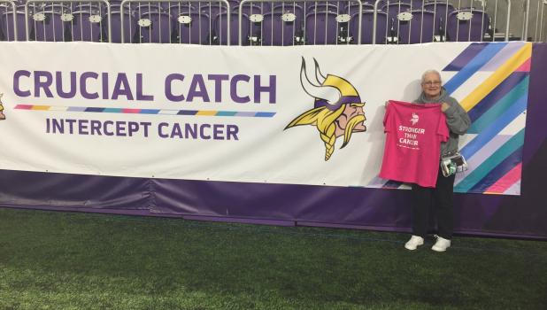 Before the Vikes game Cheryl Christensen of Staples attended the special Vikings football game Oct. 14 as a cancer survivor. She was nominated by her daughter, Shannon Badger, and they participated in the breast cancer walk around the stadium and other special events. Cheryl holds her cancer T-shirt by the cancer theme banner. (Submitted photo)
