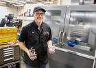 Central Lakes College machine trades instructor Jim Tyrrell shows two of the items his students have made recently, a bench vice and a small grinder. Behind him is the automated CNC machine at the college that can cut and carve materials to any shape programmed into it.